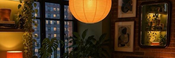 A warm apartment corner with a paper lantern and a window at dusk